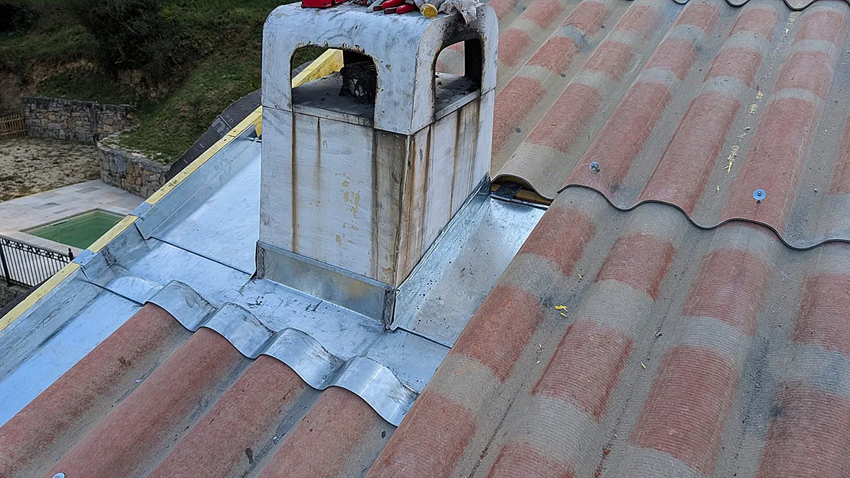 Abergement de cheminée en zinc sur une toiture en plaque sous tuile, avec piscine en arrière-plan